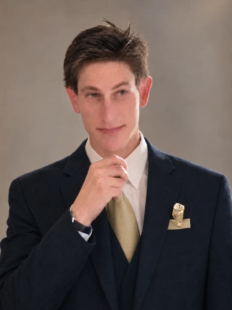 Color portrait of author Aaron Holden in a navy suit and gold tie.